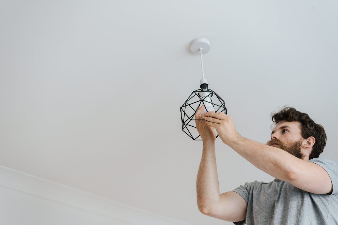why-choose-us A professional electrician skillfully installing a modern geometric ceiling lamp indoors.