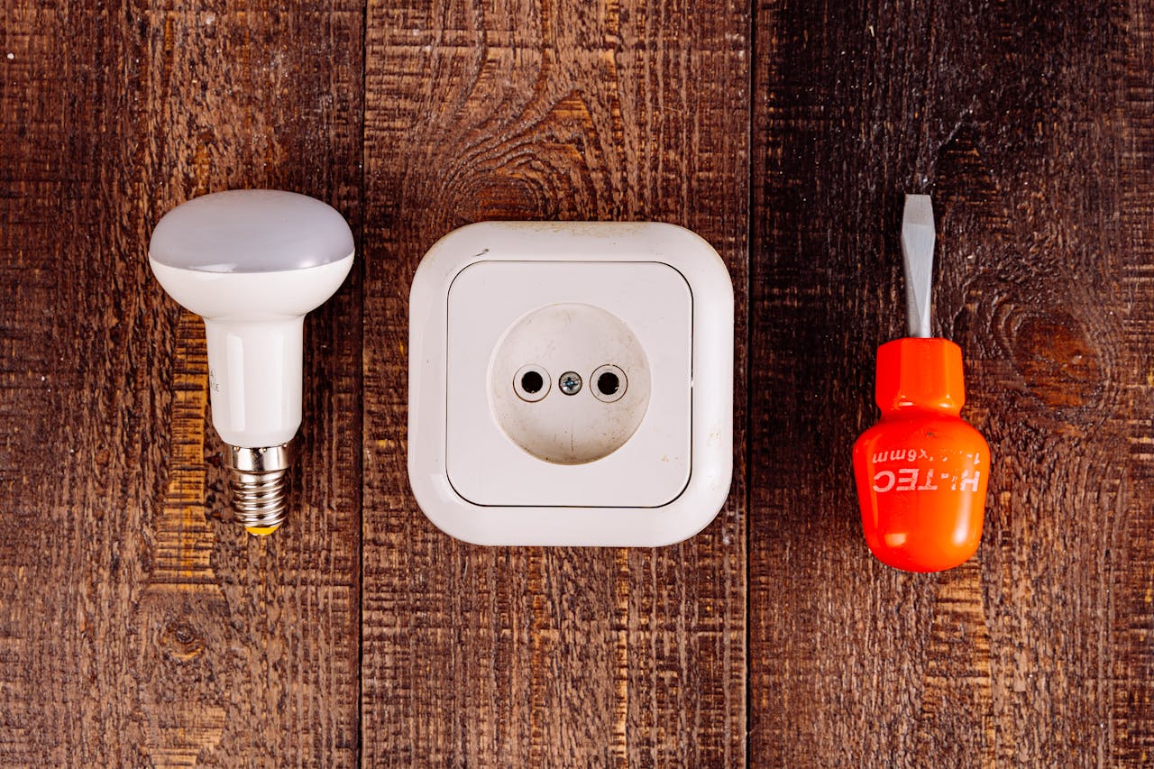 Services-03 Flat lay of a lightbulb, socket, and screwdriver on a rustic wooden surface.